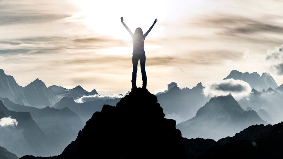 A person on a mountain summit with arms raised at sunrise