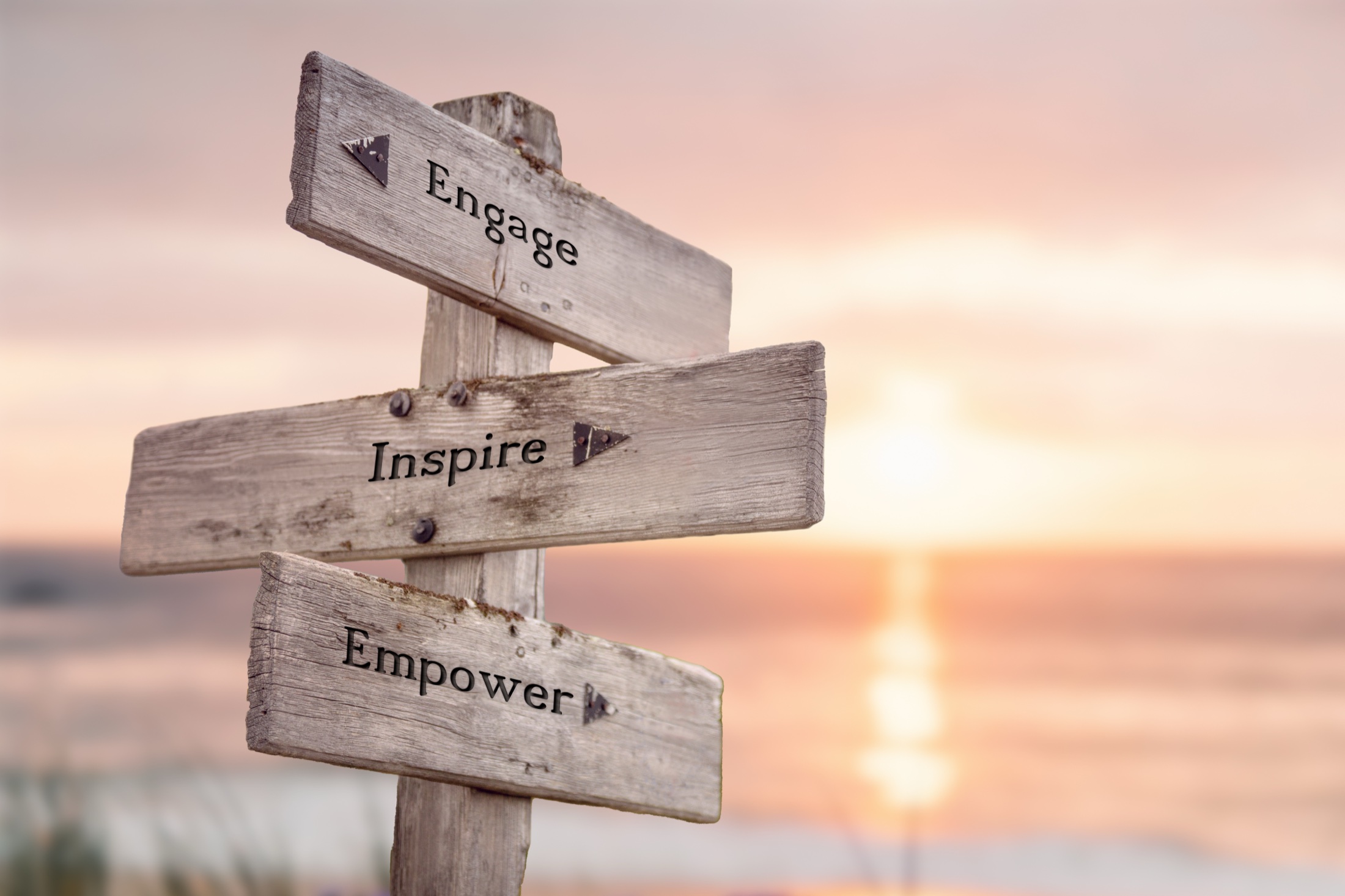 A weathered signpost at sunset reading Engage, Inspire, Empower